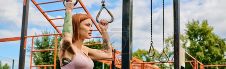 Photo for A determined woman in a pink top performs a pull-up outdoors, showing motivation. - Royalty Free Image