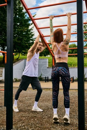 Photo for A determined woman, in sportswear, execute pull-ups side by side with a personal trainer outdoors. - Royalty Free Image
