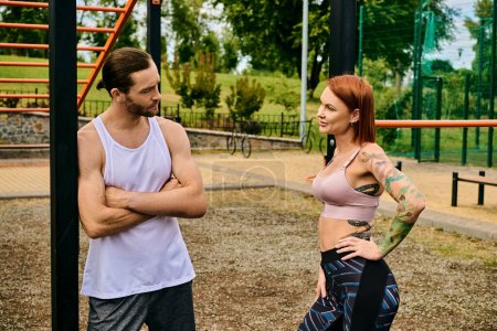 Un hombre y una mujer en ropa deportiva se paran juntos al aire libre, determinados y motivados, apoyados por un entrenamiento personal