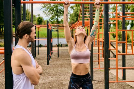A man and a woman in sportswear workout together under a clear sky in front of a gym. The personal trainer motivates her.