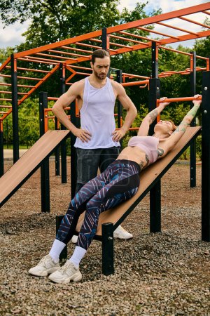 A determined man and woman in sportswear stand confidently on a wooden bench during a challenging outdoor workout session.