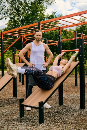 A man and woman in sportswear stand confidently on a wooden bench, showcasing determination and motivation during their outdoor exercise session.