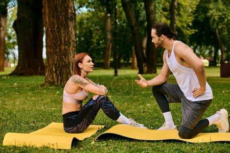 A man and woman in sportswear exercise on yoga mats in a park, guided by personal trainer.