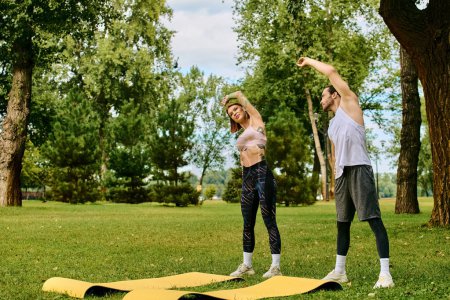A determined man and woman, both in sportswear, practice in a serene park setting, under the guidance of a personal trainer.