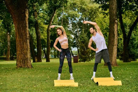 A man and woman in sportswear practice yoga together in a park, guided by a personal trainer with determination and motivation.