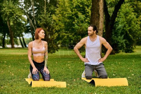 A determined man and woman in sportswear sit in the grass, guided by a personal trainer during a workout session.