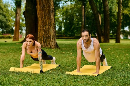 A man and a woman in sportswear perform push-ups on the grass in a park, showing determination and motivation.