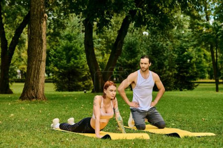 Une femme en tenue de sport pratique des poses de yoga dans un parc luxuriant guidé par un entraîneur personnel, incarnant la détermination et la motivation.