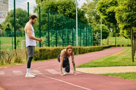 Ein Mann und eine Frau in Sportbekleidung stehen selbstbewusst auf dem Platz und zeigen mit ihrem Personal Trainer Entschlossenheit und Motivation.