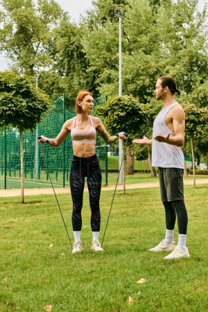 A man and a woman in sportswear exercise with determination and motivation in a vibrant park setting.