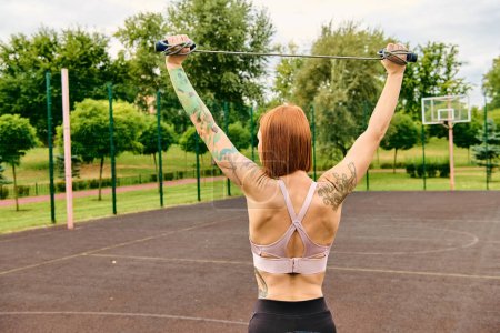 A determined woman in sportswear holding a skipping rope in a park, embodying motivation and strength.