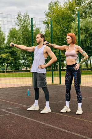 Ein Mann und eine Frau in Sportkleidung, die mit Hanteln trainieren und beim gemeinsamen Training Entschlossenheit an den Tag legen