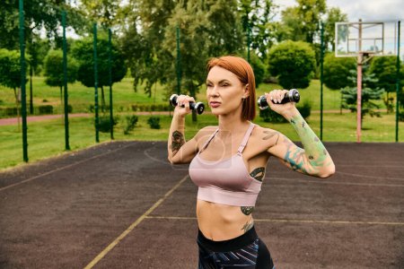 A woman in sportswear, holds a pair of dumbbells with determination and focus during outdoor exercise.