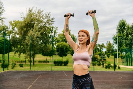 A determined woman in sportswear holding two dumbbells in a vibrant parking lot