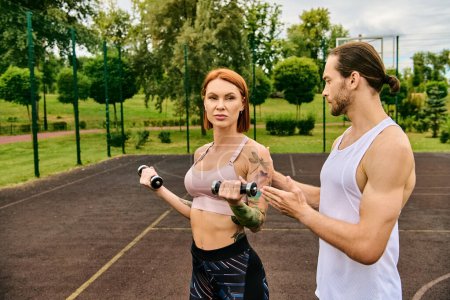 Photo for A determined man and woman in sportswear exercising together with dumbbells outside - Royalty Free Image