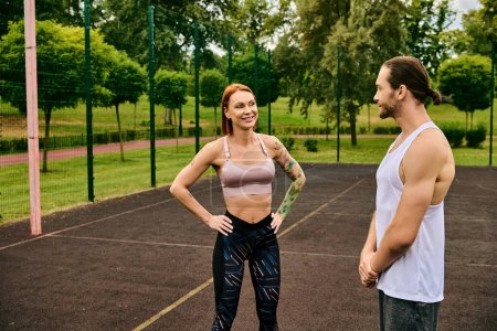Ein Mann und eine Frau in Sportbekleidung stehen auf einem Tennisplatz bereit und zeigen mit ihrem Personal Trainer Entschlossenheit und Motivation.
