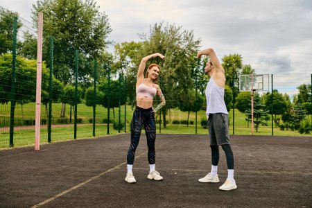 Un hombre y una mujer en ropa deportiva están en la parte superior de una cancha de baloncesto, mostrando su determinación y motivación mientras hacen ejercicio