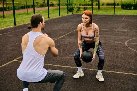 A man and a woman in sportswear workout with ball, coached by a personal trainer outdoors.