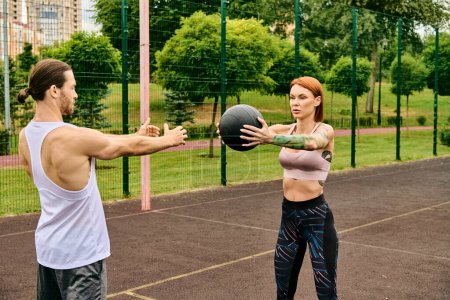 Un hombre y una mujer en ropa deportiva se ejercitan juguetonamente con una pelota al aire libre, mostrando determinación y motivación.