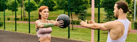 Un homme et une femme en vêtements de sport jouent activement avec une balle à l'extérieur sous la direction d'un entraîneur personnel.