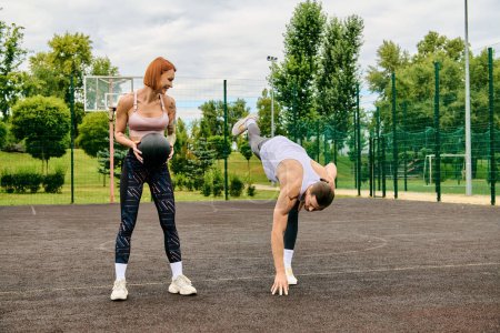 Eine entschlossene Frau trotzt der Schwerkraft mit einem Ball und zeigt Kraft und Gleichgewicht, während ihr persönlicher Trainer zuschaut.