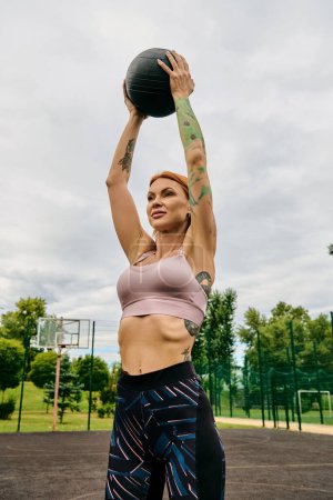 A woman in sportswear, holding a medicine ball, trains outdoors