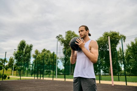 Téléchargez les photos : Un homme en tenue de sport tient une balle sur le terrain, faisant preuve de détermination et de motivation pour le match à venir. - en image libre de droit