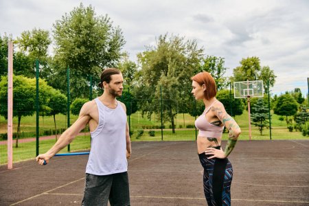 A man and woman, both in sportswear, stand on a court, showcasing determination and motivation in outdoor workout session.