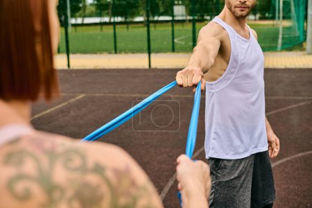 Photo for A man in sportswear confidently holds a blue resistance band with woman - Royalty Free Image