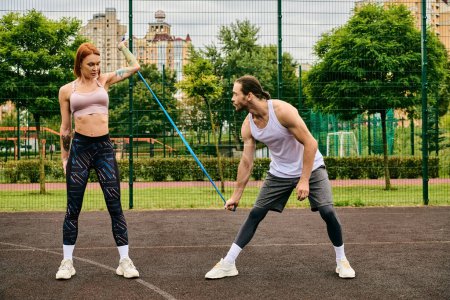 A man and a woman, both in sportswear, are fiercely working out on a sunny outdoor court.