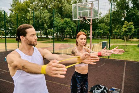 A man and a woman in sportswear having resistance band training with determination and motivation outdoors.