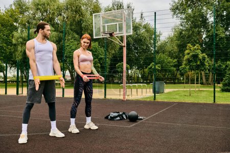 A man and a woman, in sportswear, stand on a basketball court during resistance band training