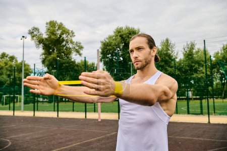 Athletic man holding a yellow resistance band on a court outside