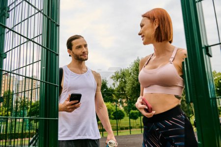 Ein Mann und eine Frau in Sportbekleidung turnen gemeinsam im Freien und halten ihr Smartphone in der Hand