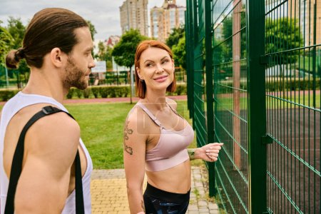 Photo for A man and woman in sportswear standing next to a fence, exuding determination and motivation after outdoor exercise - Royalty Free Image