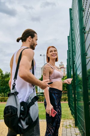 Foto de Un hombre y una mujer decididos en ropa deportiva se paran junto a una valla después del entrenamiento - Imagen libre de derechos