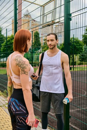A determined man and woman in sportswear stand together outdoors by a fence,