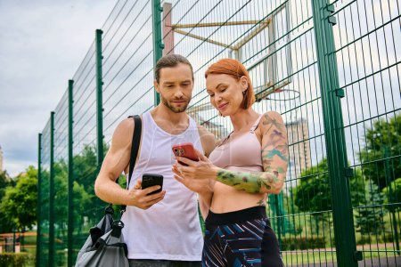 A man and a woman in sportswear, check their progress on a cell phone.
