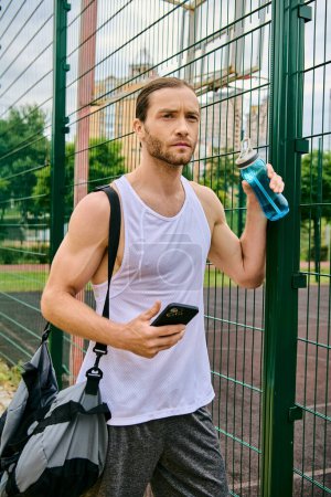 Téléchargez les photos : Un homme se tient à côté d'une clôture, tenant un téléphone portable, absorbé dans son contenu. - en image libre de droit