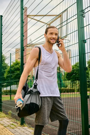 Foto de Un hombre con atuendo casual está al lado de una valla teniendo una conversación en su teléfono celular. - Imagen libre de derechos