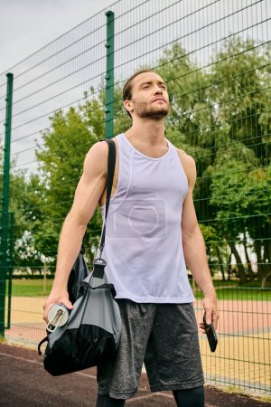 A determined man in sportswear walks down a tennis court, holding a bag
