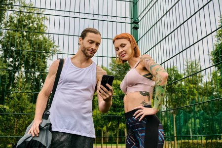 Foto de Un hombre y una mujer en ropa deportiva se paran uno al lado del otro, después de hacer ejercicio al aire libre, teléfono inteligente - Imagen libre de derechos