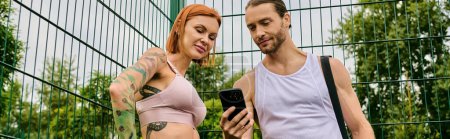 Un homme et une femme en vêtements de sport se tiennent ensemble à l'extérieur, en utilisant un smartphone