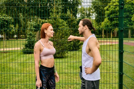 A man and a woman in sportswear stand together in front of a fence after their outdoor exercise session.
