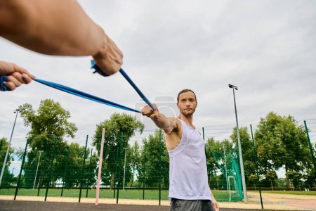Ein Mann hält selbstbewusst ein Widerstandsband in der Hand, während er auf einem lebhaften Tennisplatz steht.