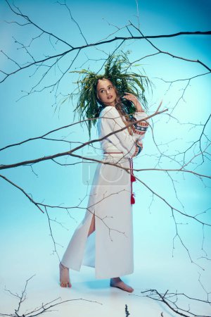 Eine junge Mavka im weißen Kleid hält anmutig einen zarten Zweig in einem skurrilen Studio-Setting.