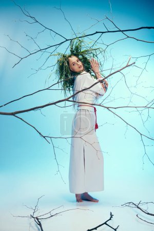 Une jeune mavka en tenue traditionnelle se tient gracieusement devant une branche d'arbre tordue dans un décor de studio de fées et de fantaisie.