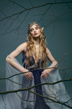 A fairy-like young woman in a beautiful blue dress standing gracefully in front of a majestic tree in a fantasy-inspired studio setting.