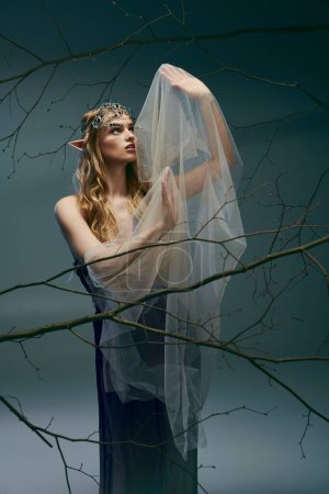 A young woman dressed as an elf princess stands gracefully in front of a majestic tree wearing a veil.