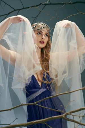 Eine junge Frau in einem blauen Kleid mit Schleier über dem Kopf, die in einem Atelier eine Aura von Fee und Fantasie ausstrahlt.